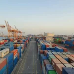 Pelabuhan sibuk dengan tumpukan kontainer kargo berwarna-warni saat matahari terbenam, menggambarkan aktivitas ekspor impor